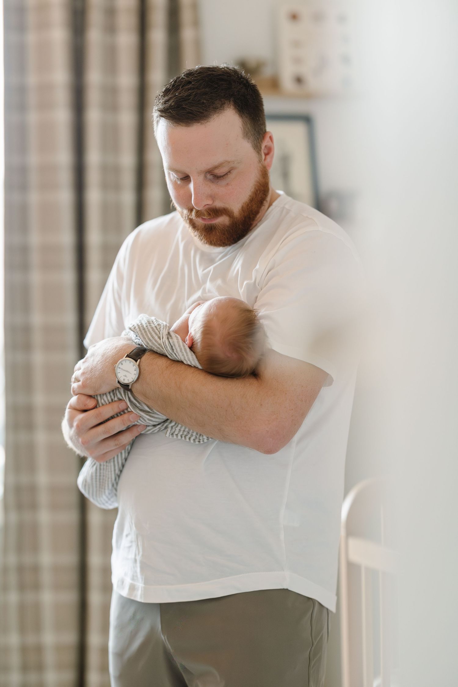 A parent in a white shirt tenderly holds and gazes down at a sleeping newborn baby wrapped in striped fabric.