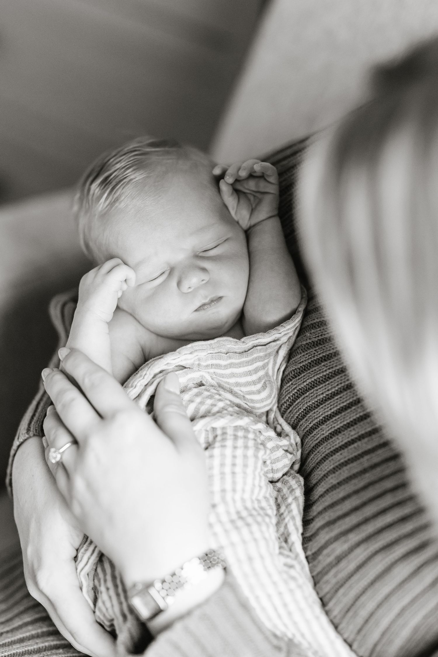 A sleeping newborn baby in a striped onesie being gently cradled in black and white photography.