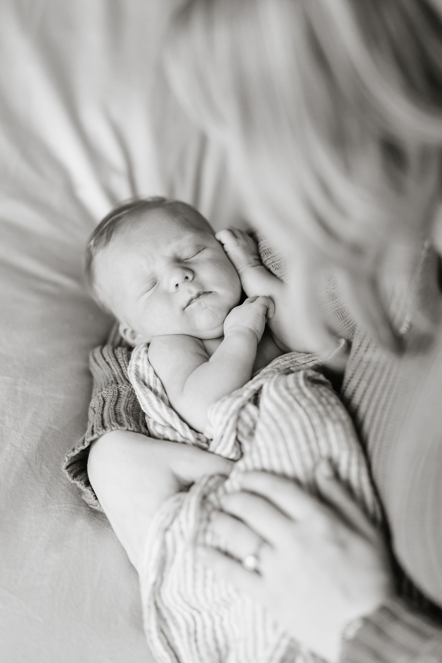 A black and white artistic photo series of a sleeping baby in soft striped clothing laying on white bedding.