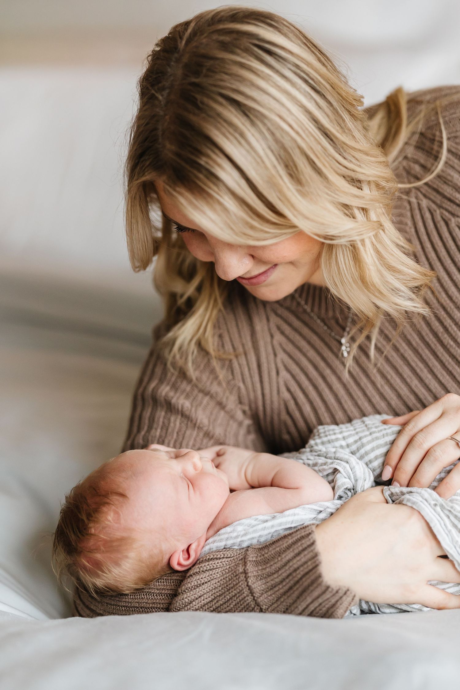 A tender moment between parent and newborn baby lying together on white bedding in natural light.
