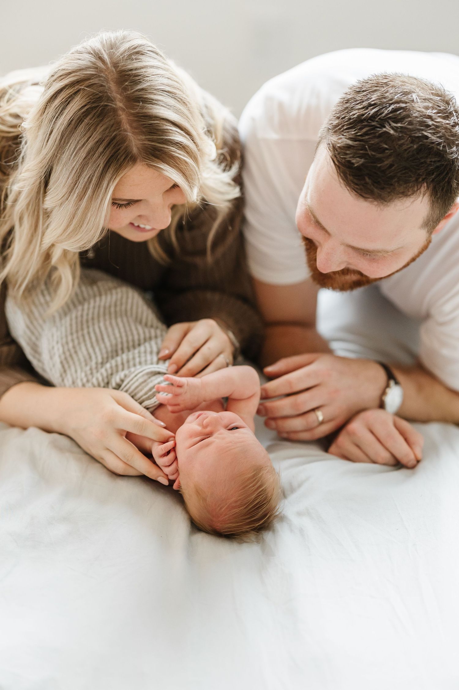 A loving couple tenderly cuddles with their newborn baby in a series of intimate black and white photographs.