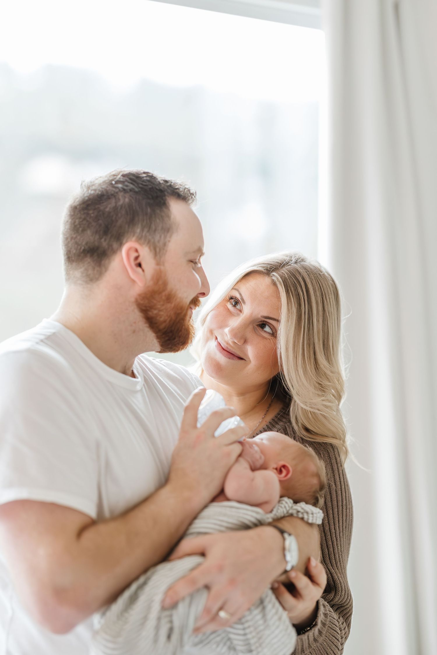 A couple shares intimate moments in a bright white room while wearing casual white clothing.