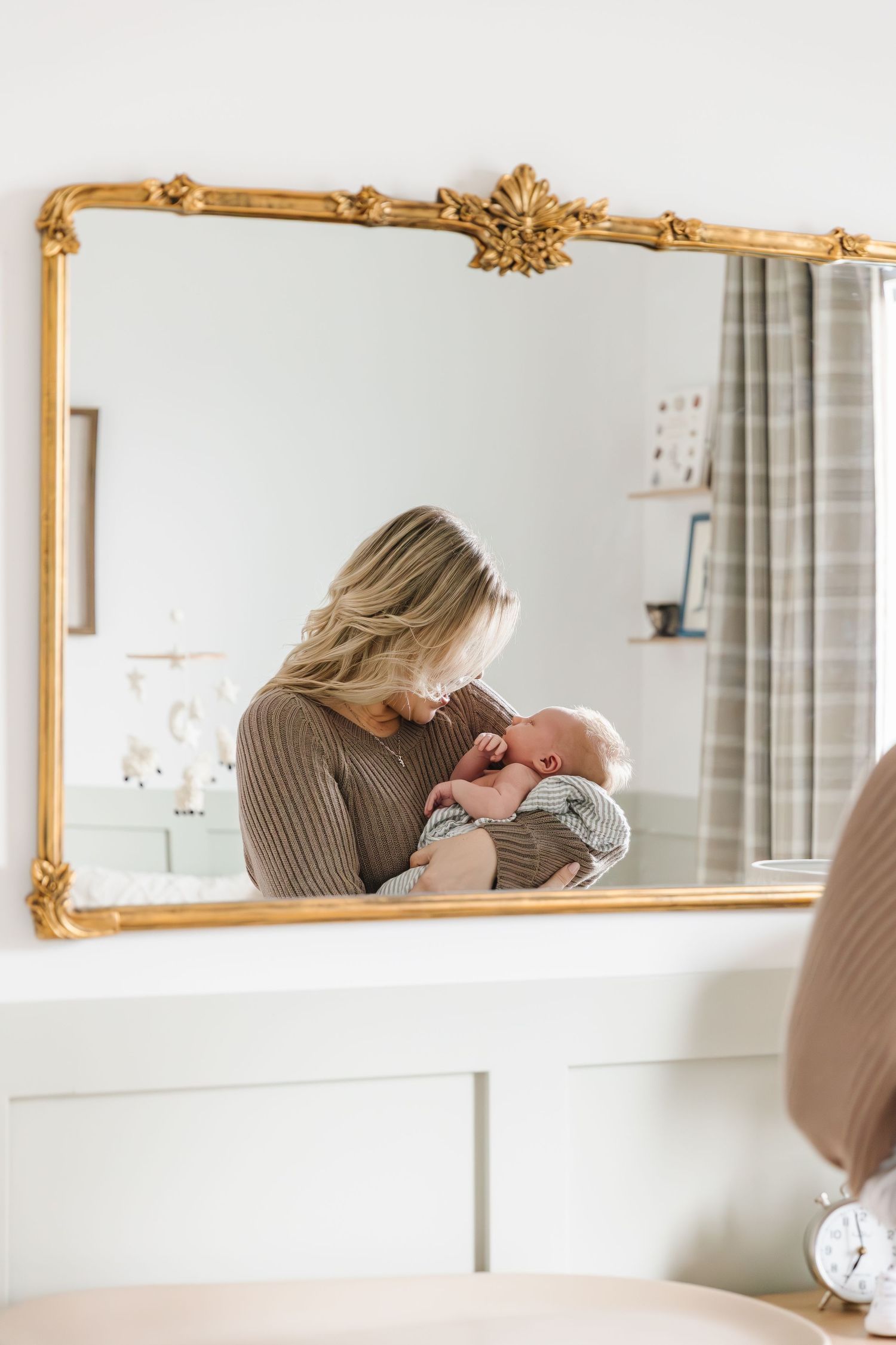 Elegant gold-framed mirror mounted on white wall reflects interior decor in bright room.