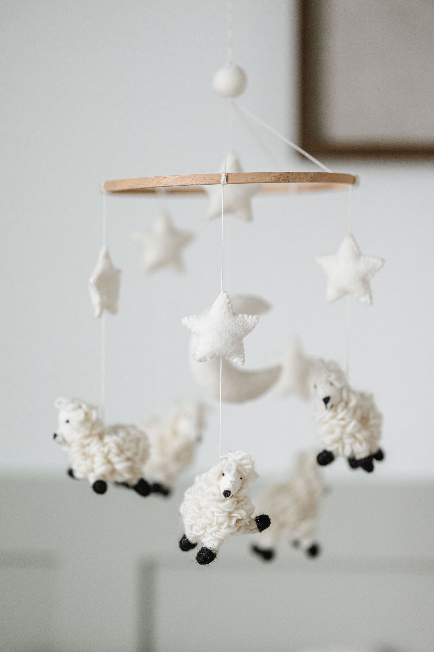A nursery mobile with white fluffy sheep and stars hanging from a wooden circular frame against a light background.