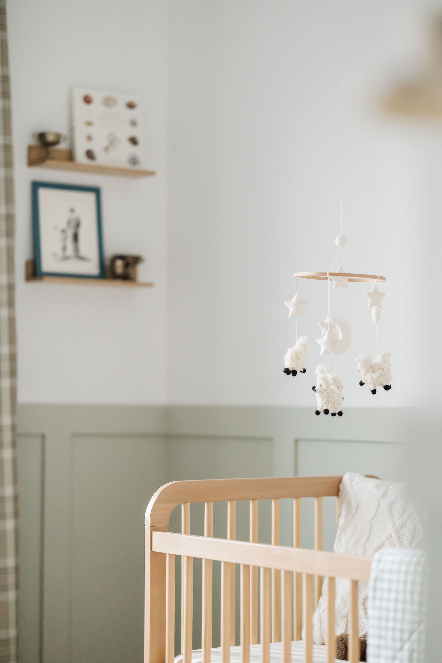 A wooden baby crib with a delicate sheep and star mobile hanging above in a minimalist nursery setting.