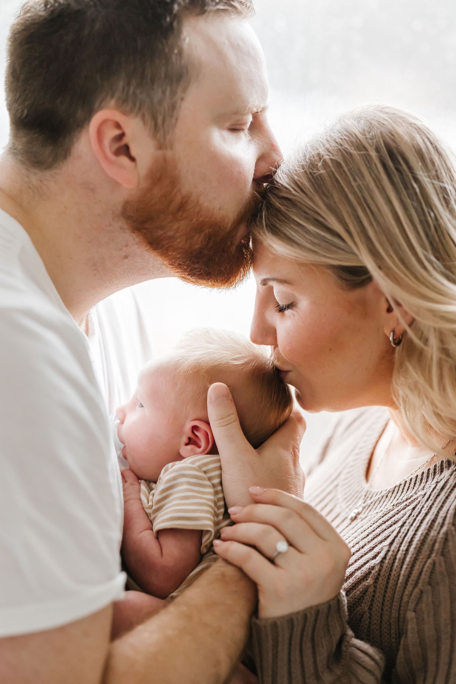 An intimate family portrait with a newborn baby in soft natural window light.