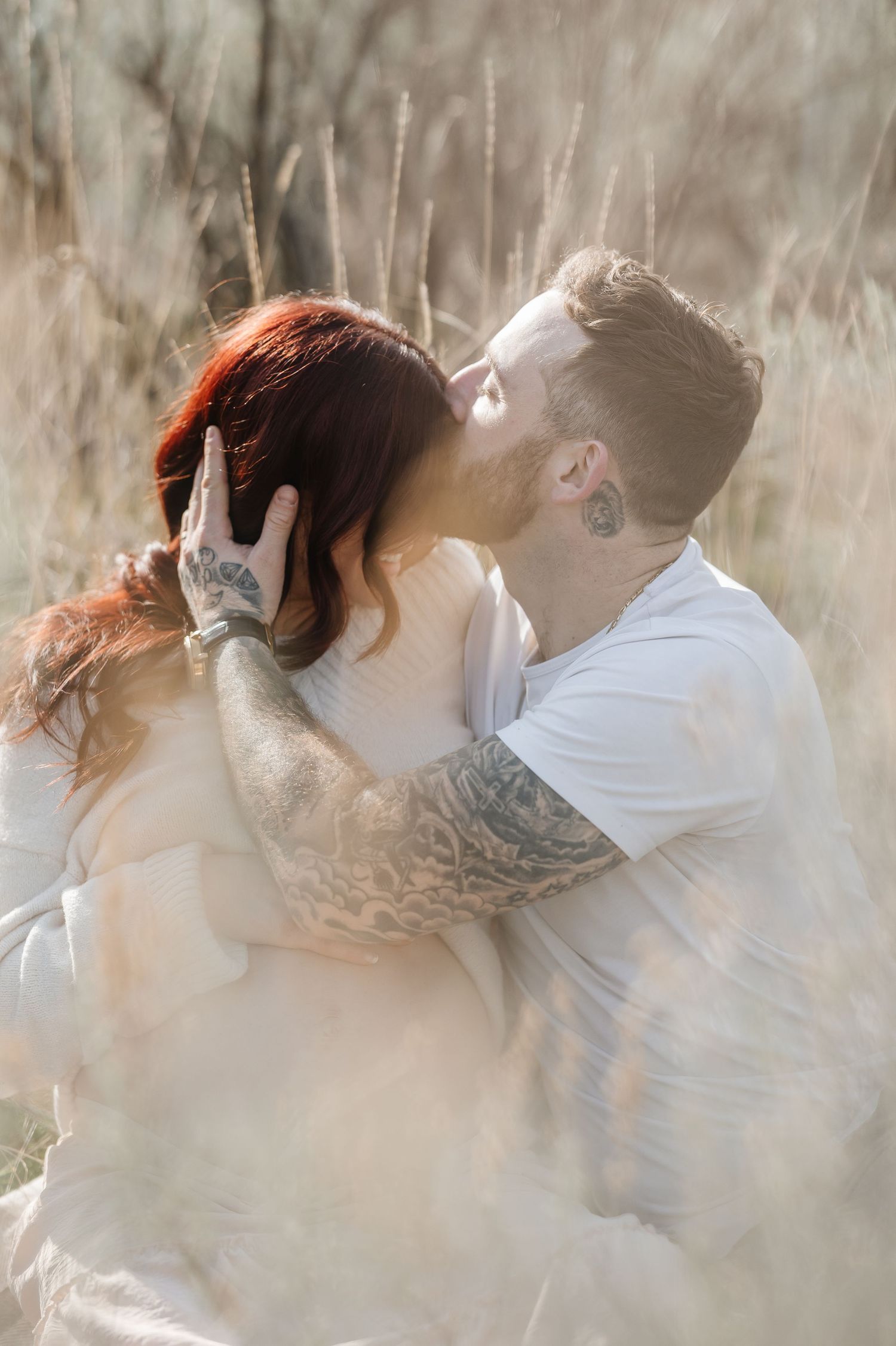 A romantic couple sharing an intimate kiss in a sunlit field of tall grass with dreamy atmospheric lighting in Kelowna BC