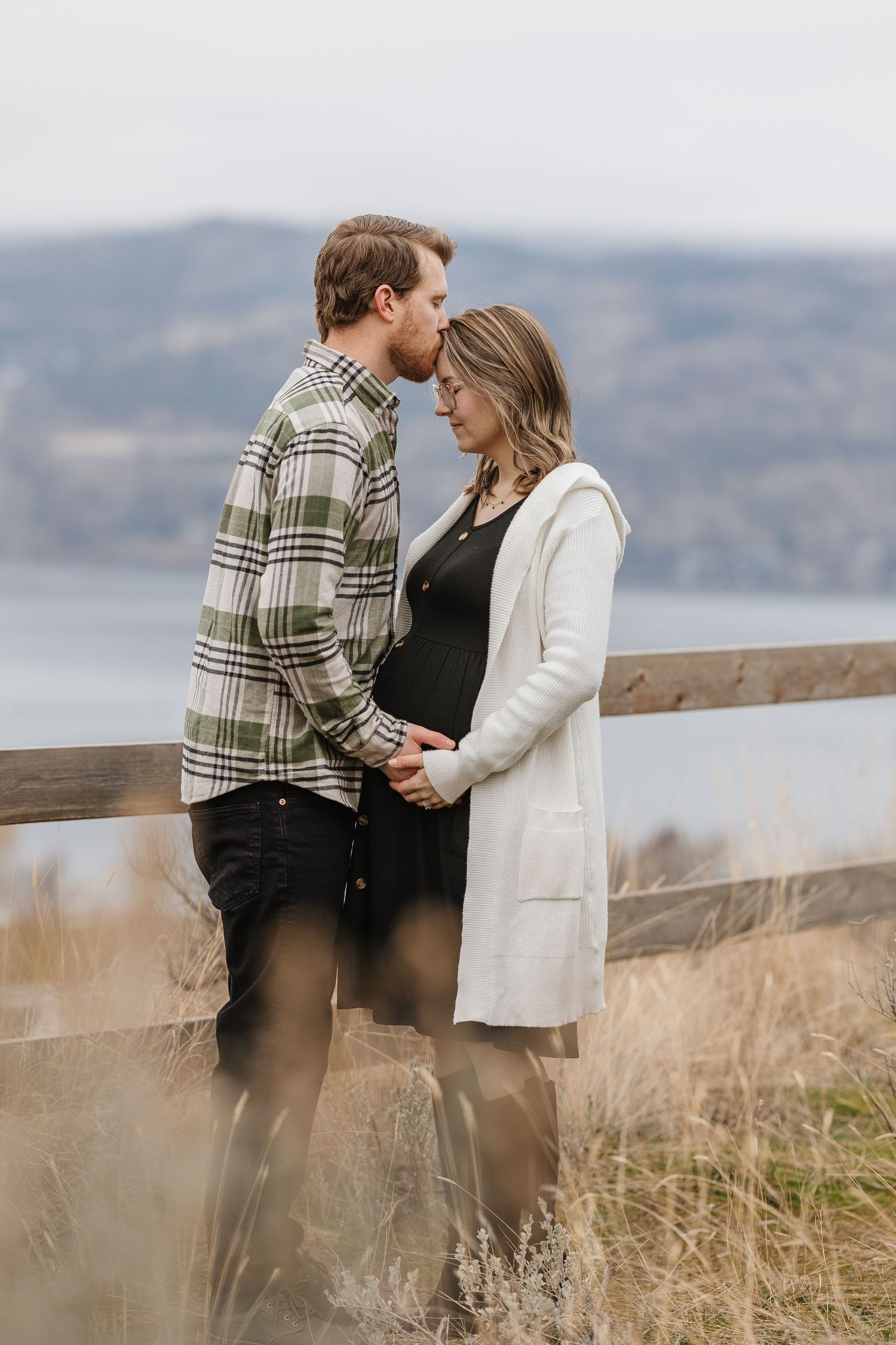 A couple shares an intimate moment on a hilltop overlooking Okangan lake, with mountains in the background at Knox mountain park in kelowna