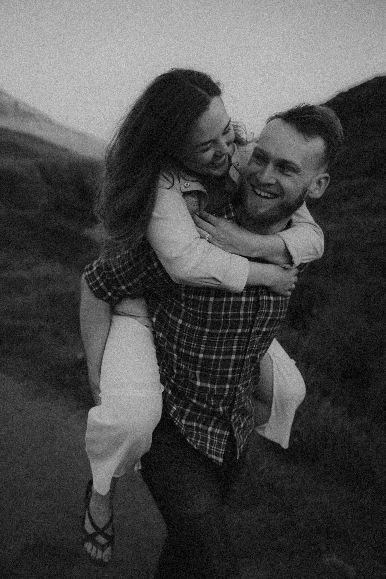 A joyful couple shares a piggyback ride moment in black and white photography.