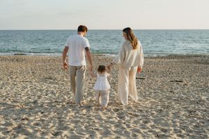 Family walking along the shoreline at sunset wearing coordinated white and cream outfits.