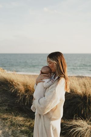 Intimate family embraces on a beach with tall grass and ocean backdrop.