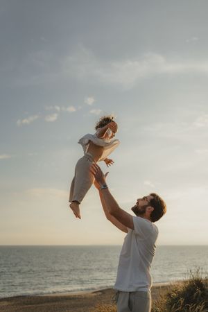 Playful moments between parent and child against ocean horizon at sunset.