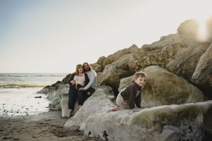 a couple sat on rocks at a Dorset beach watching their child climb