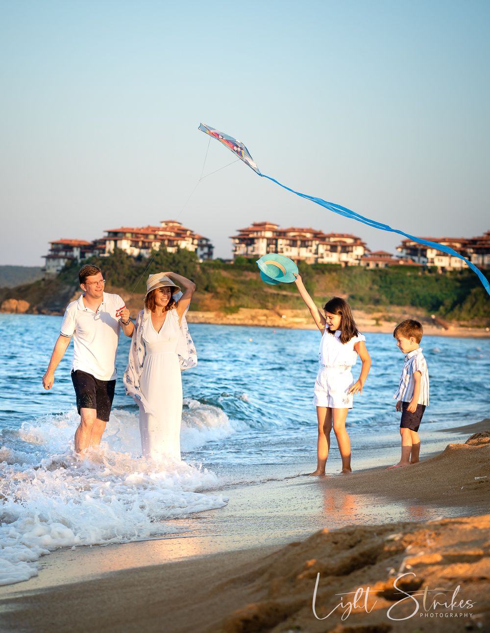 Family photographer captured a family enjoying a beach day together on a with a kite flying overhead and coastal homes in the background.