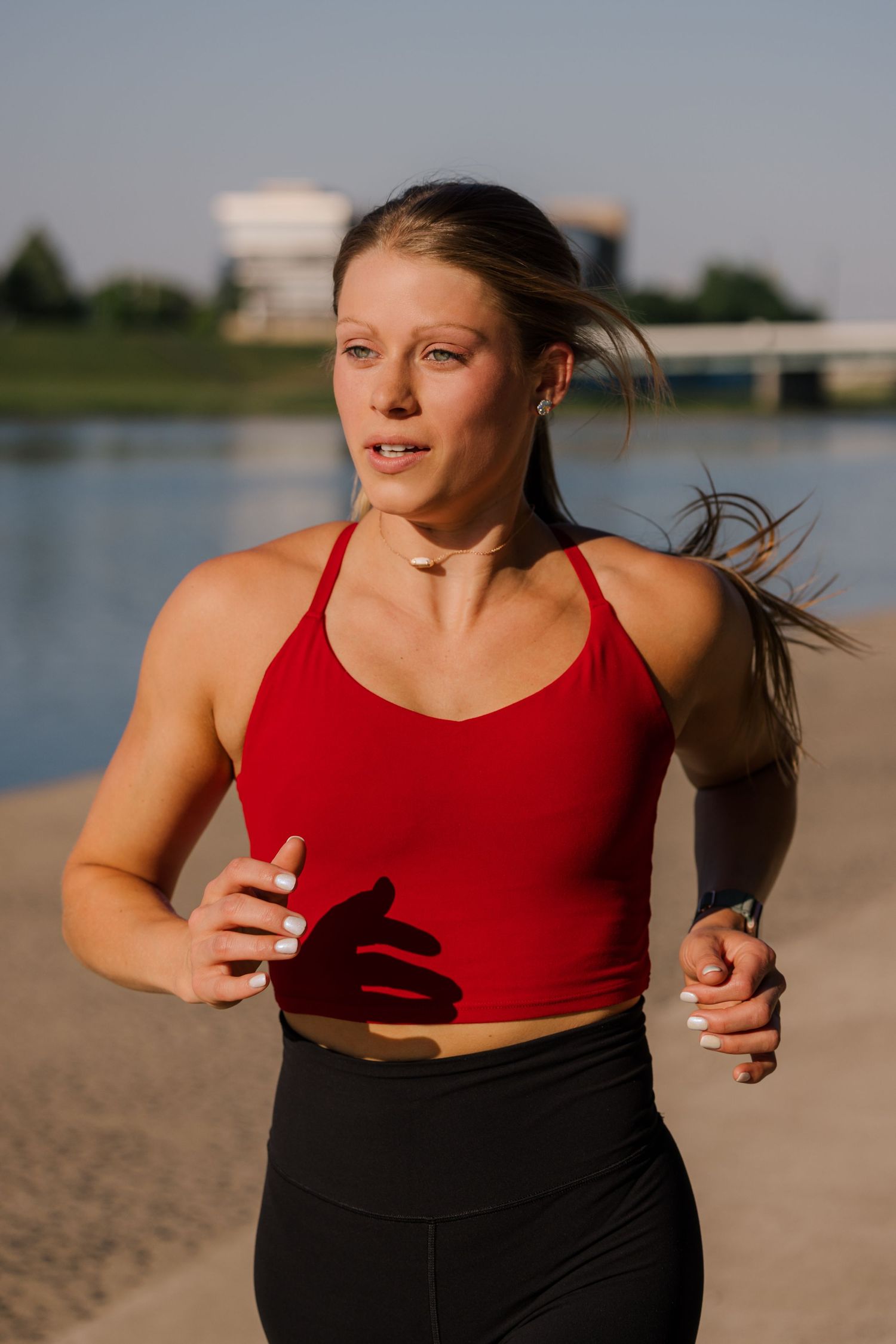 Runner in red tank top and black leggings exercises during golden hour near a lake.