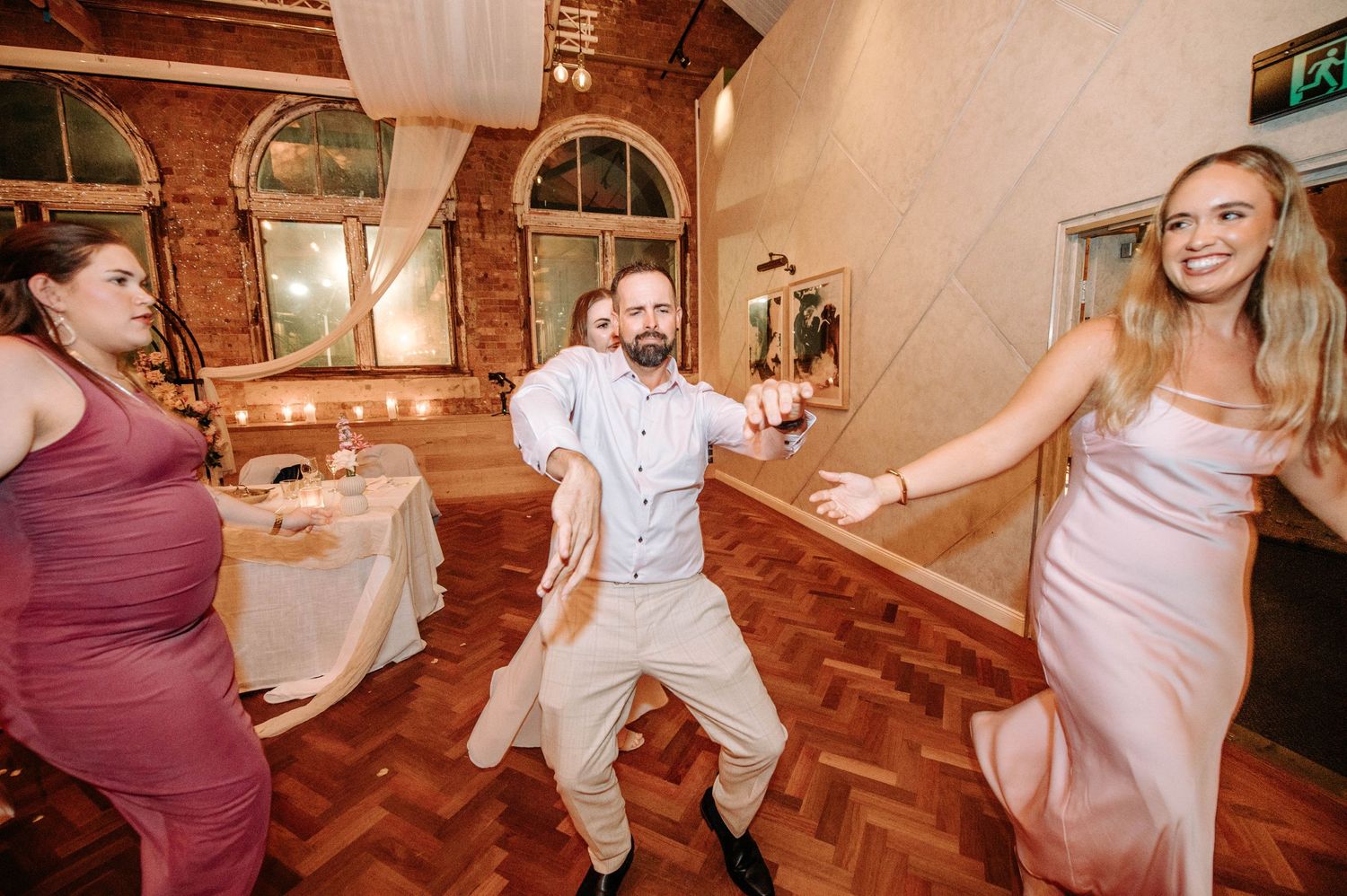 Energetic wedding guests dancing and having fun on a parquet floor at an indoor reception.