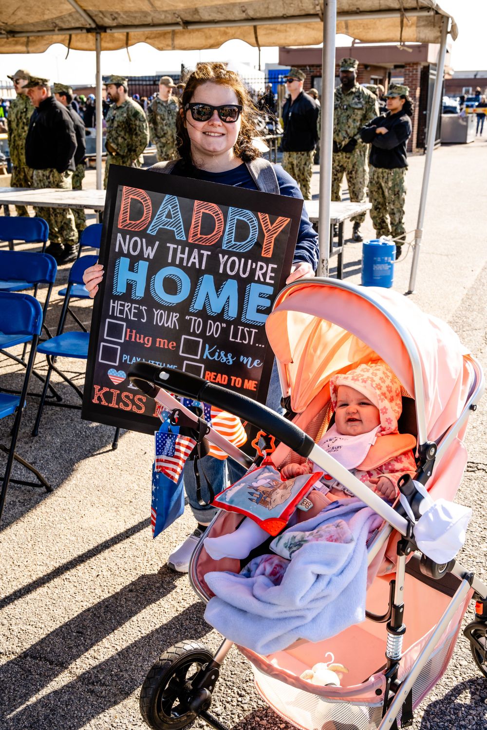 Welcome sign and stroller displayed at military homecoming event on sunny day.
