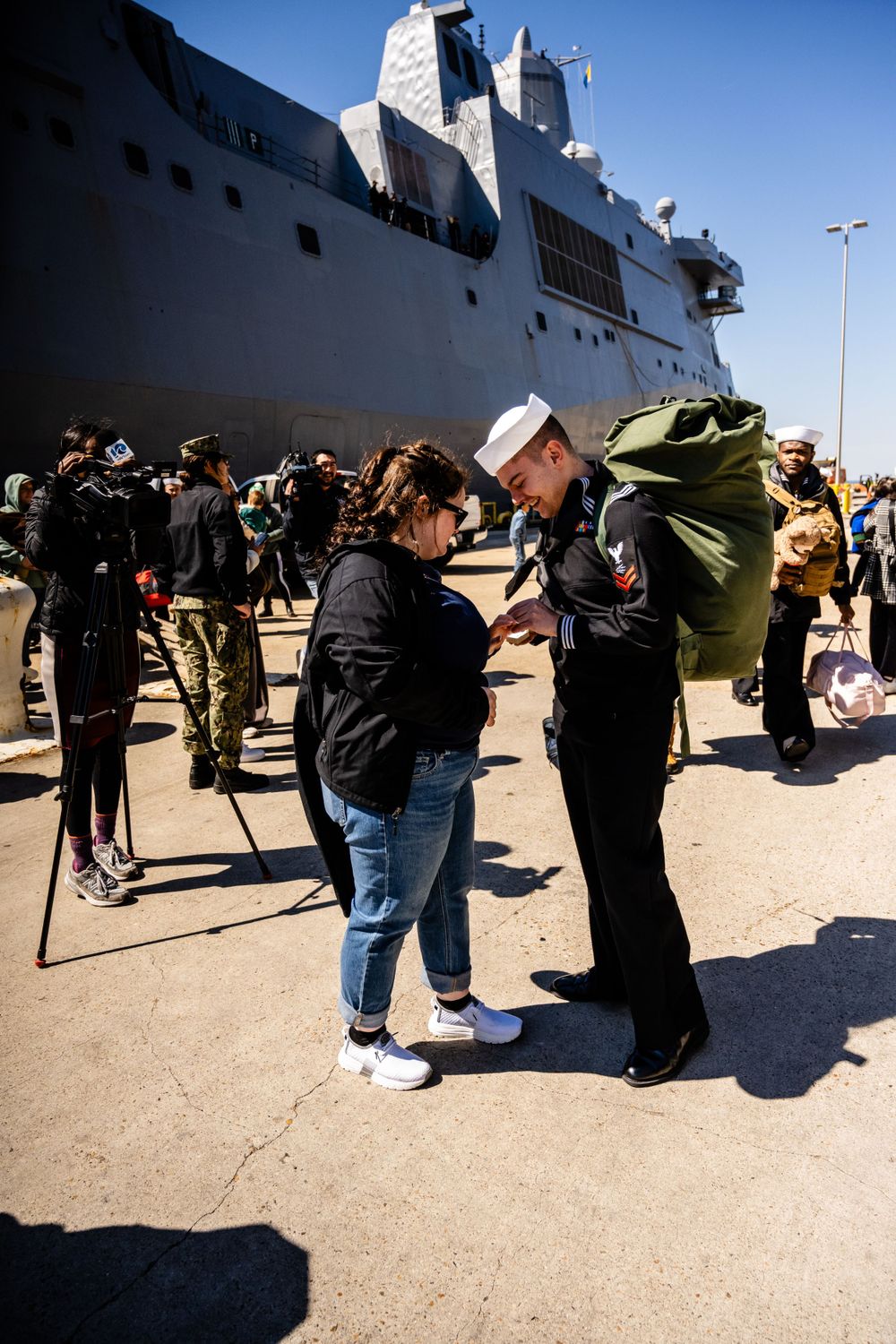 Touching scene at military homecoming with naval ship in background.