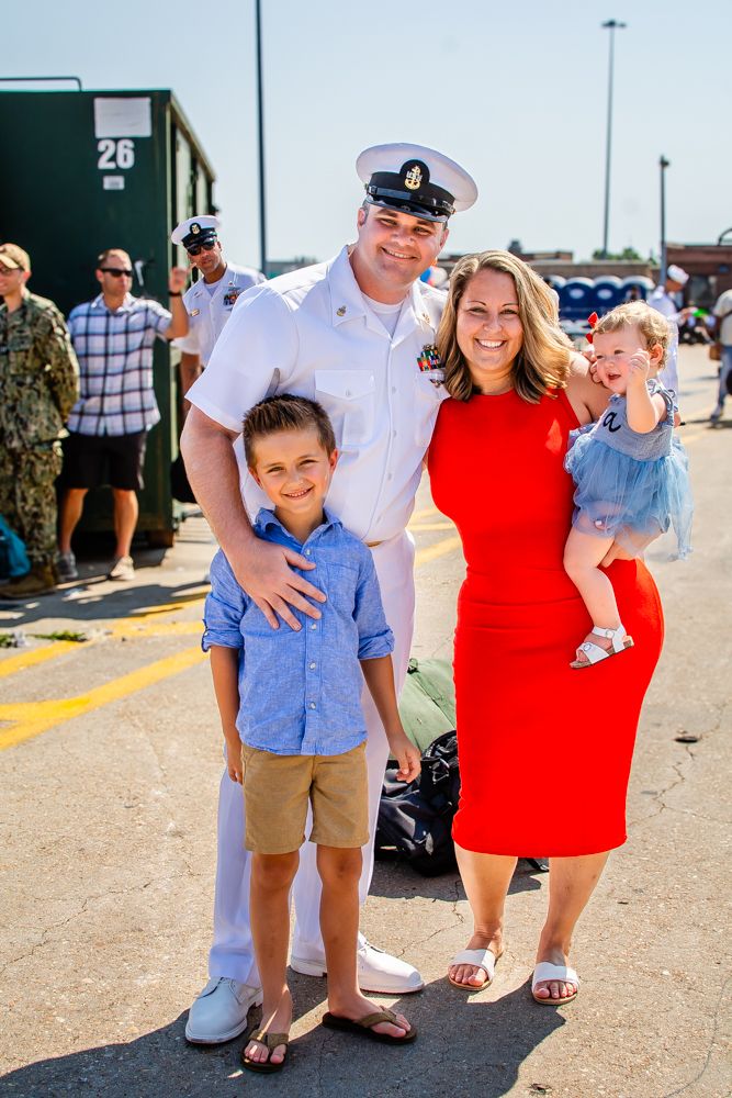 Military family poses together during homecoming celebration at naval base.