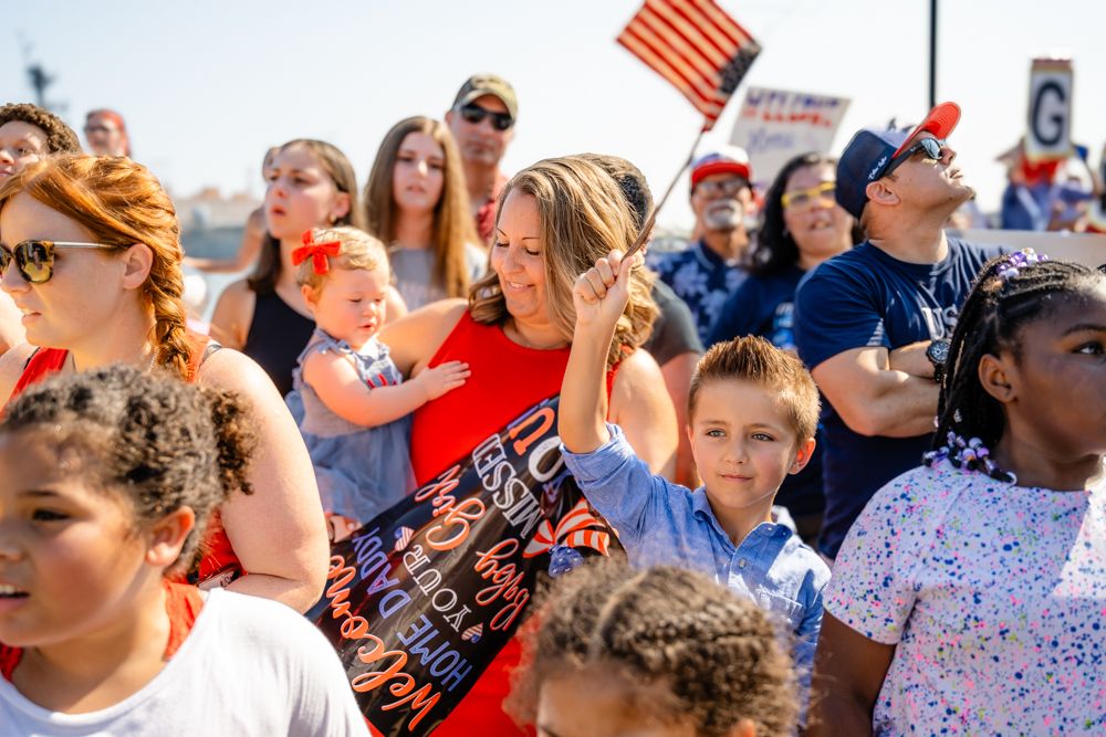 A crowd gathers outdoors waving American flags during a patriotic celebration.