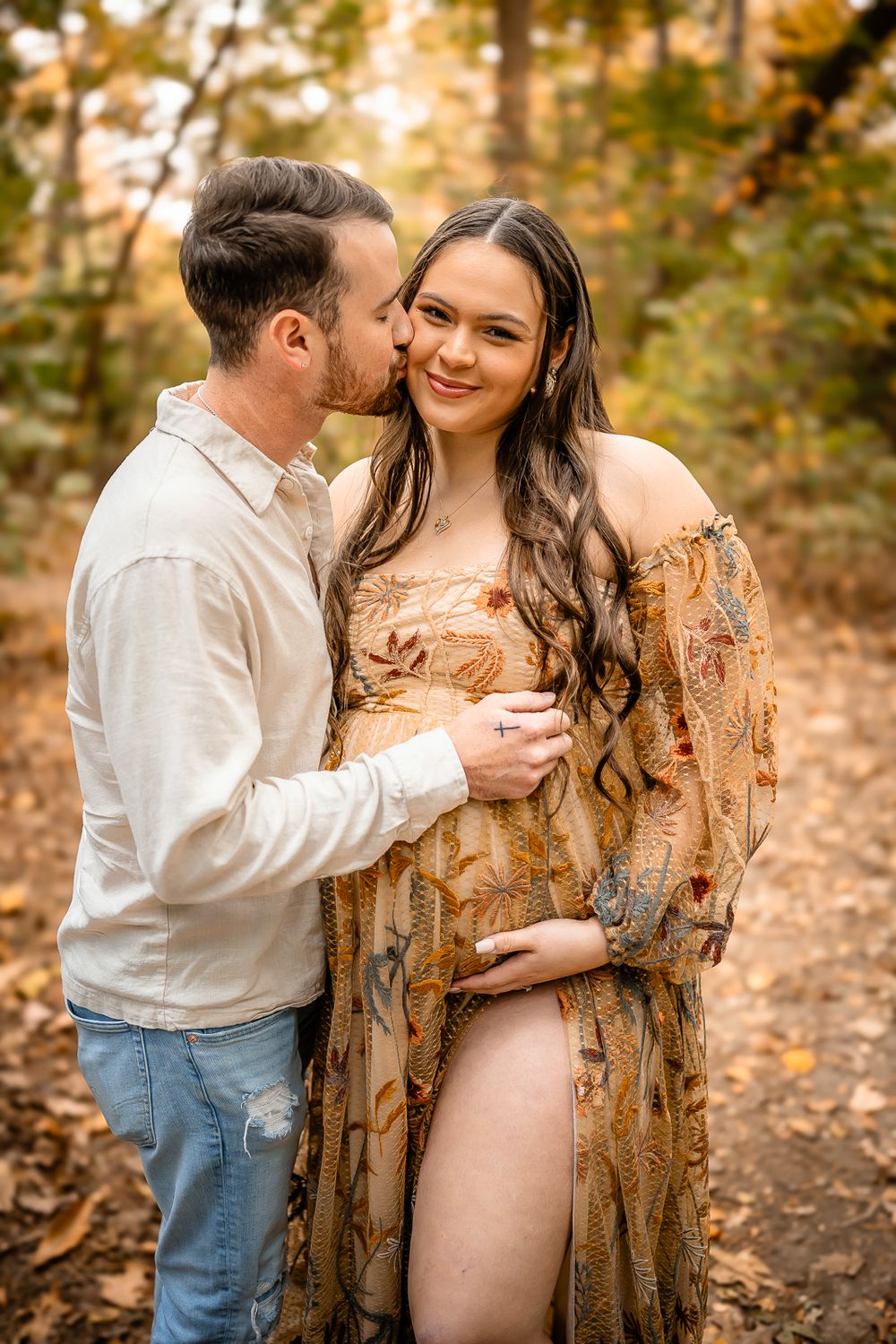 A romantic couple embracing in a sunlit forest wearing coordinated neutral tones.