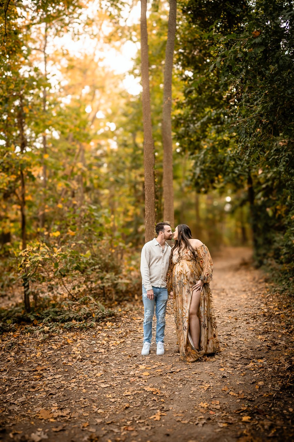 A romantic couple on a leaf-covered forest path during golden hour.
