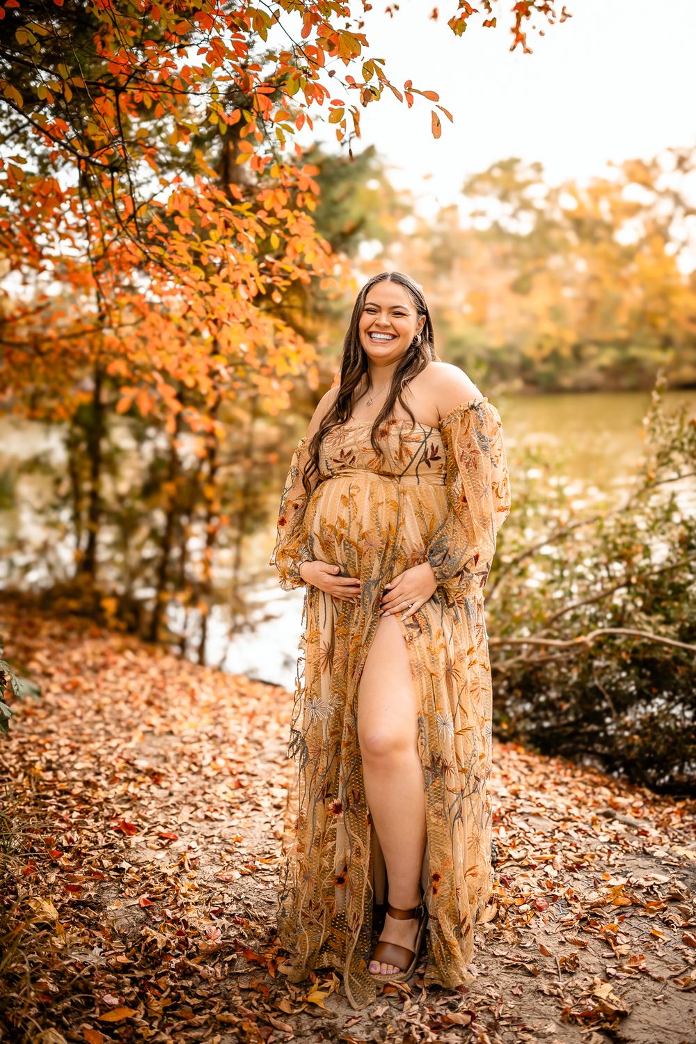 A maternity portrait featuring a flowing tan dress against vibrant fall foliage.