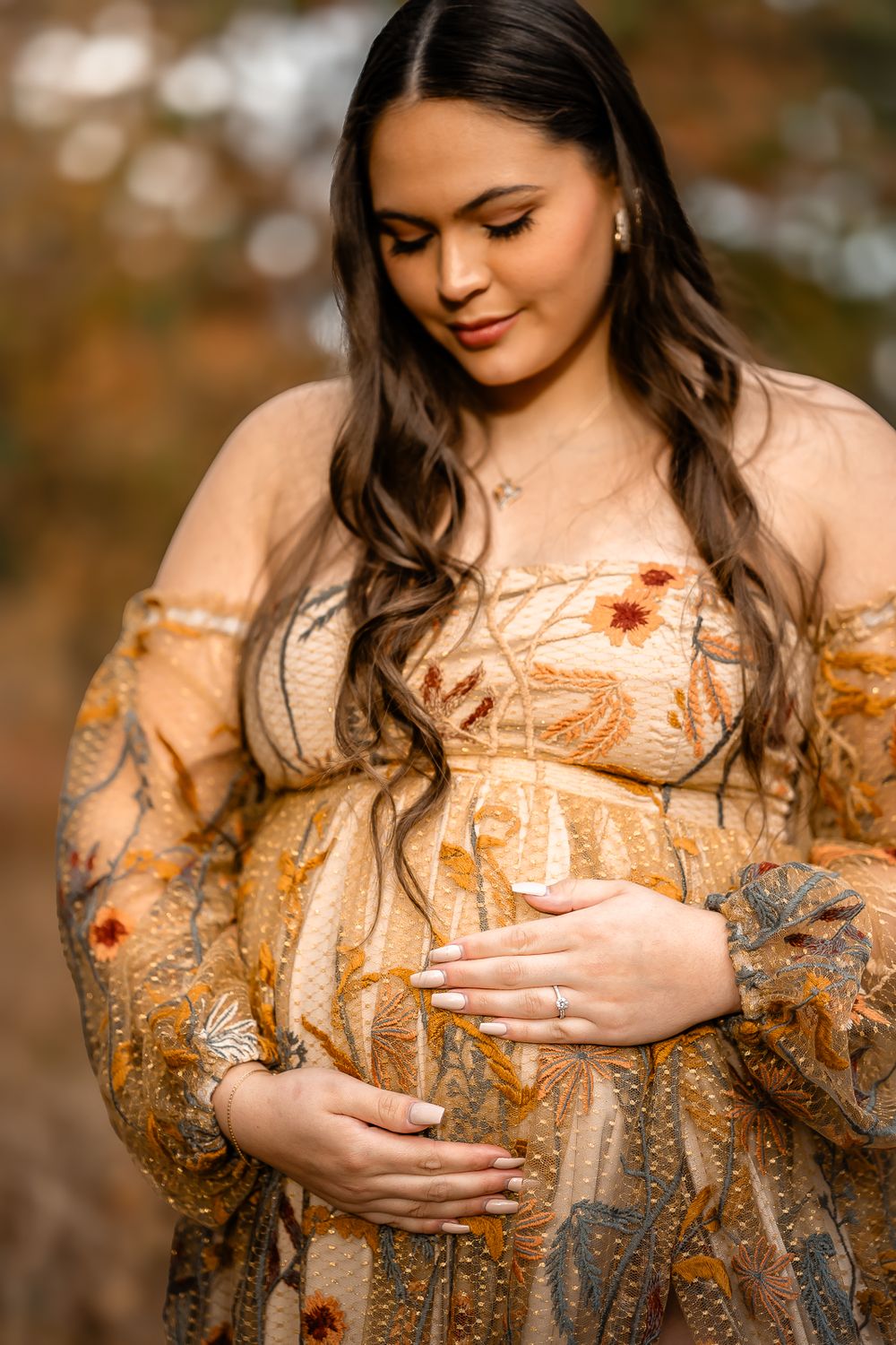 Close-up maternity portrait showcasing a golden floral dress in warm autumn lighting.