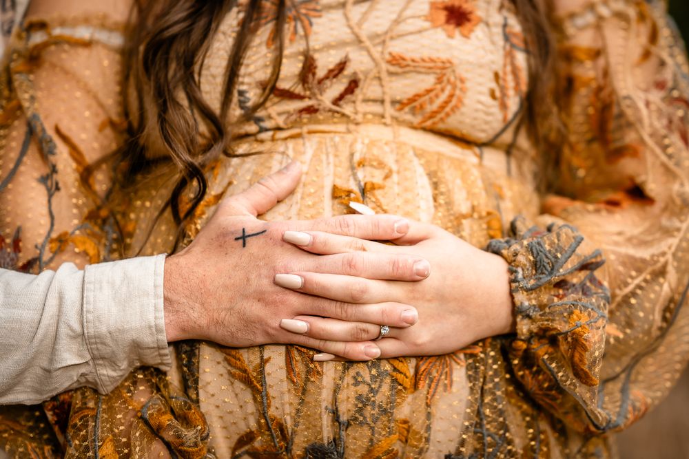 Close-up shot of hands resting on belly through golden floral fabric during maternity shoot.