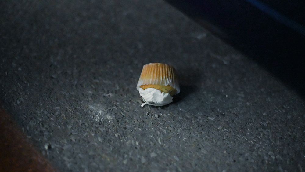 Close-up of a golden cupcake wrapper on dark asphalt surface.