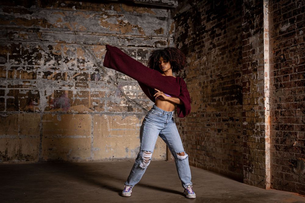 performance photography Brighton photo of a dancer in an abandoned building wearing jeans and a red jumper. stone wall in the background
