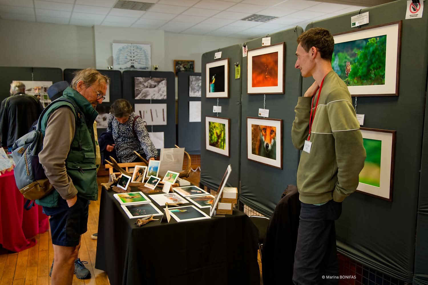 Photography exhibition booth displaying various framed images on black grid wall panels.