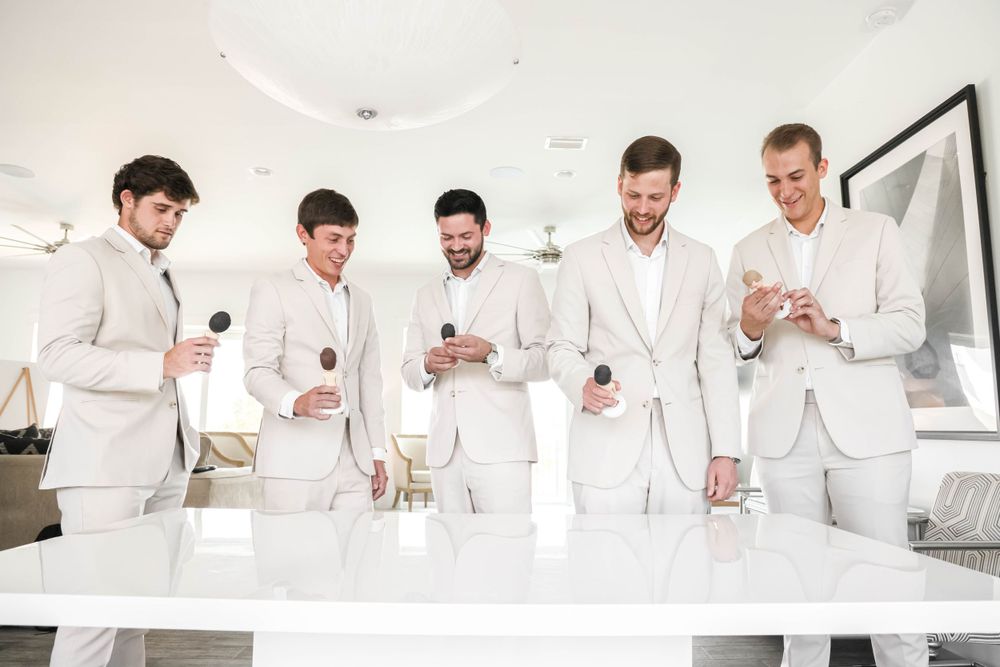 Groomsmen in crisp white suits checking their phones while getting ready.