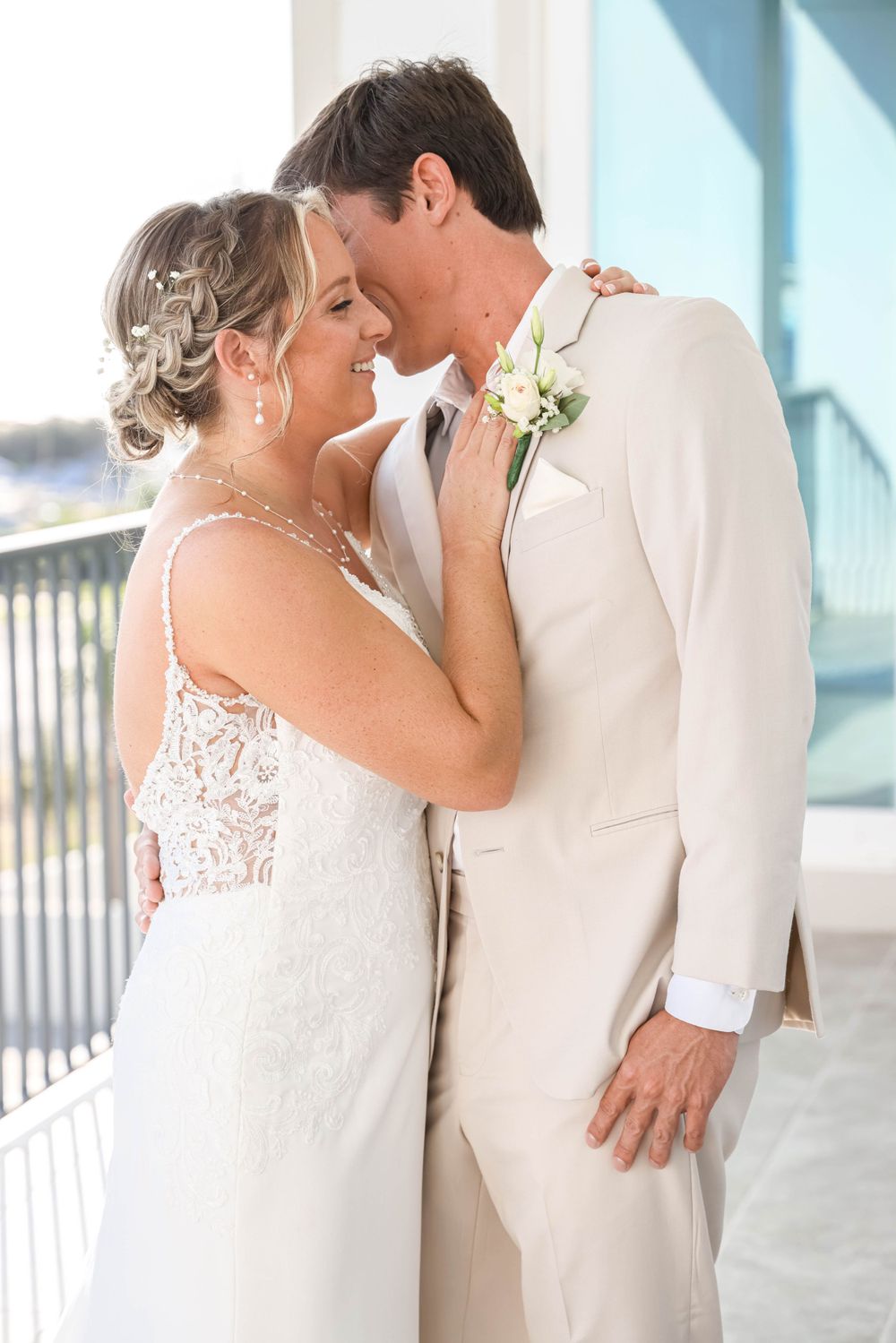 A romantic embrace between newlyweds on a white balcony overlooking the water.