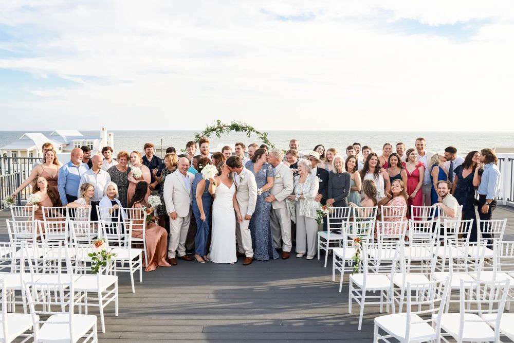 Wedding ceremony setup on an outdoor deck with white chairs and floral arch overlooking the water.