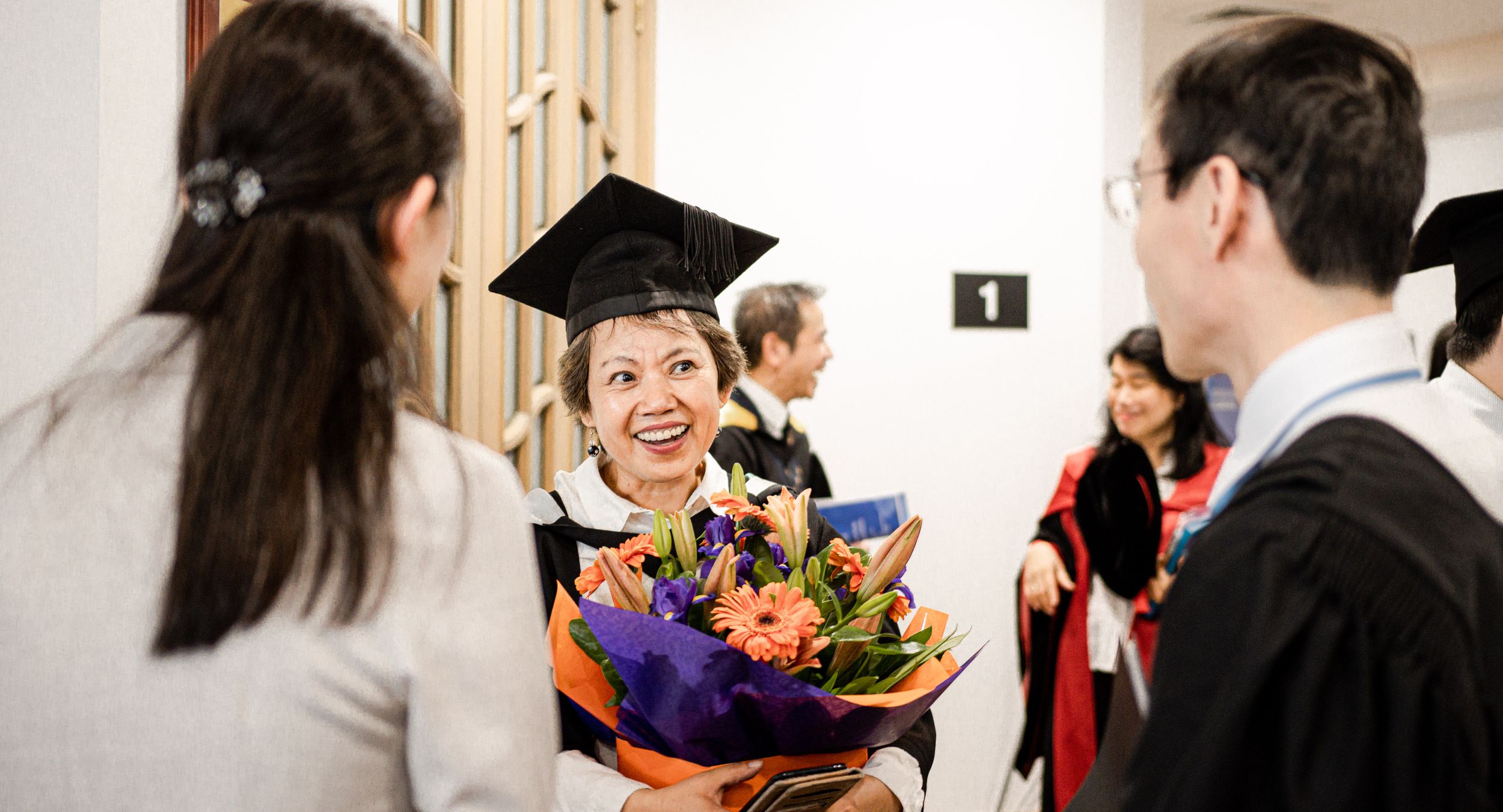 Graduate celebrating with flowers and diploma during graduation ceremony.