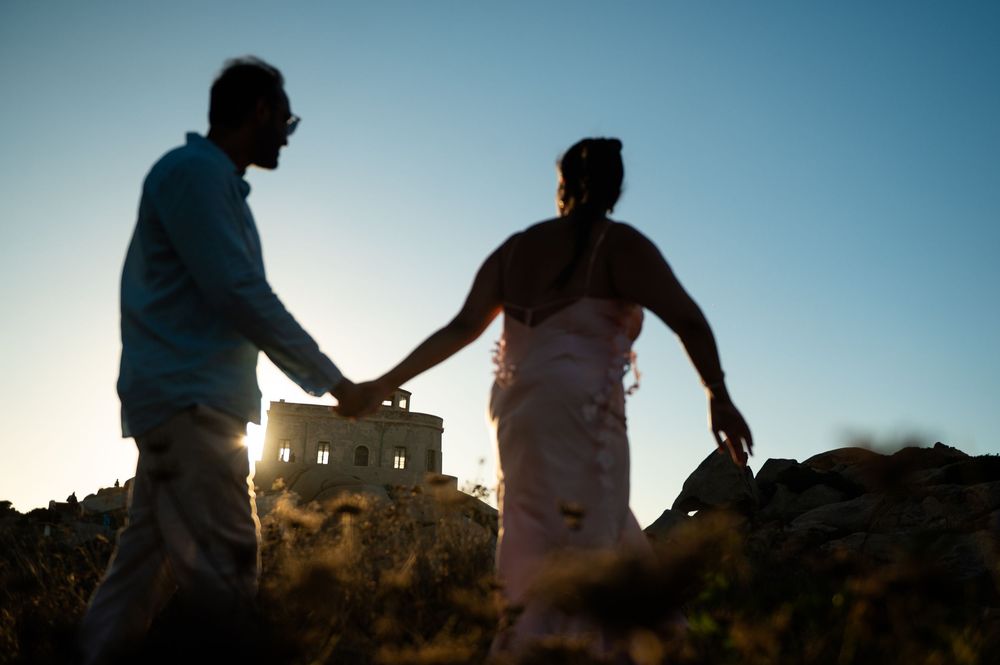 Silhouette of a couple holding hands at sunset with a historic building in the background.
