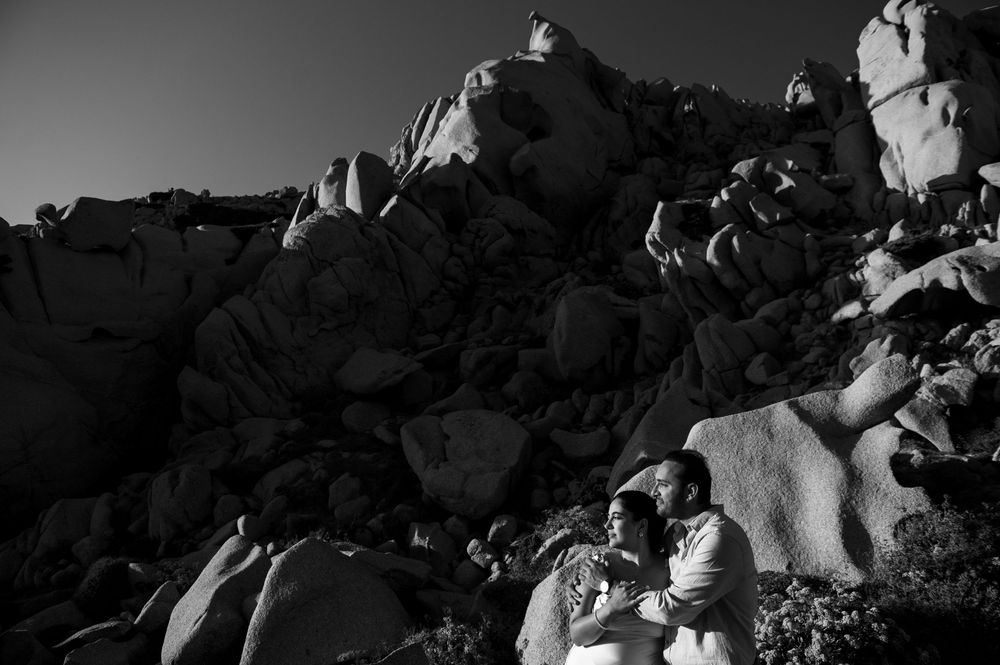 Black and white photo of a couple embracing among dramatic rocky boulders in a desert landscape.