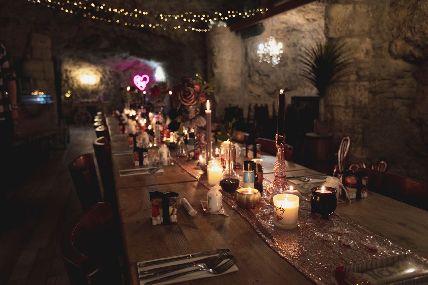 Rustic underground dining setup with candlelight and string lights creating ambiance.
