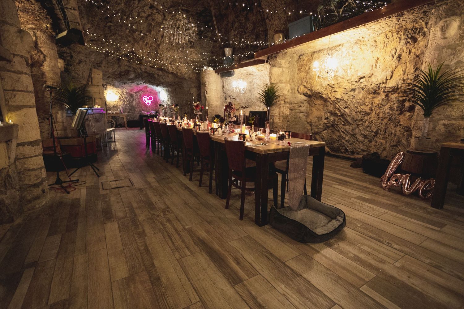 Long banquet table set in a stone cave with romantic lighting and rustic decor.