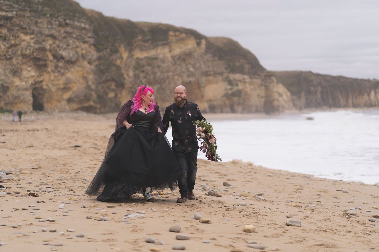 Two figures walking along a dramatic coastal beach with towering cliffs.
