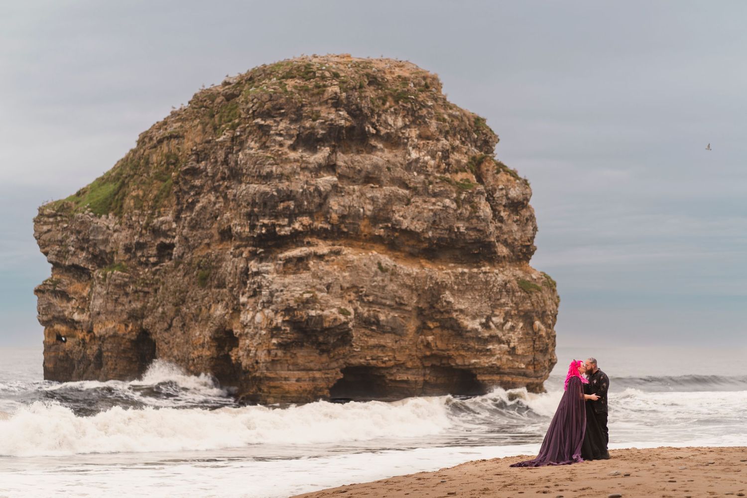 A dramatic black gown stands out against a massive coastal rock formation.