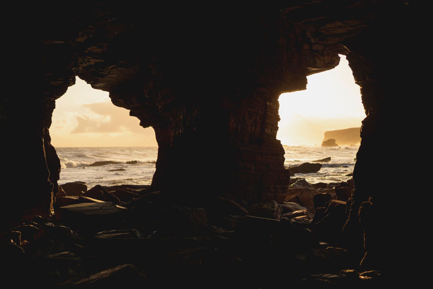 View of ocean waves through two cave openings at sunset creating natural window frames.