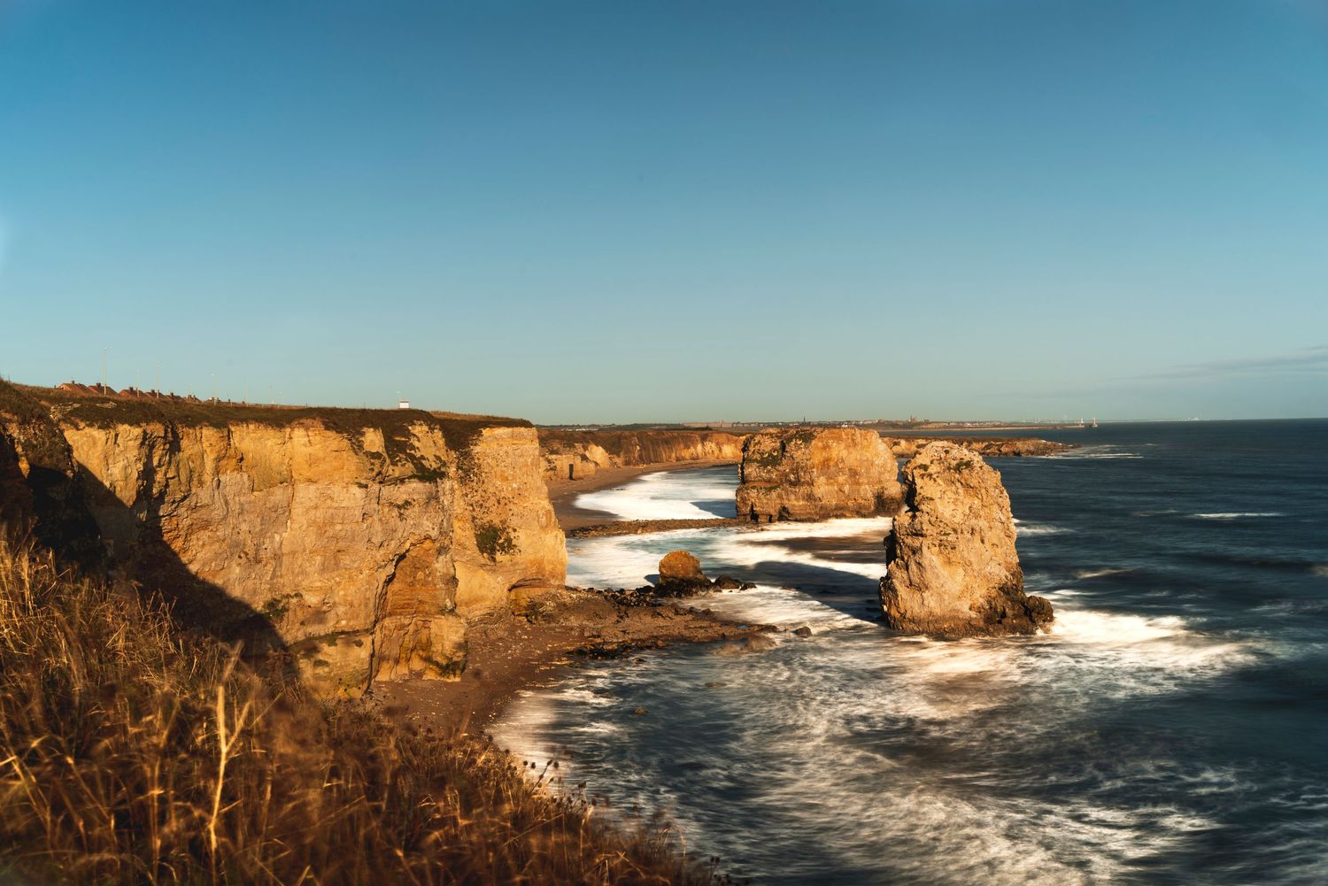 Dramatic coastal landscape with golden limestone cliffs and crashing waves along the ocean.
