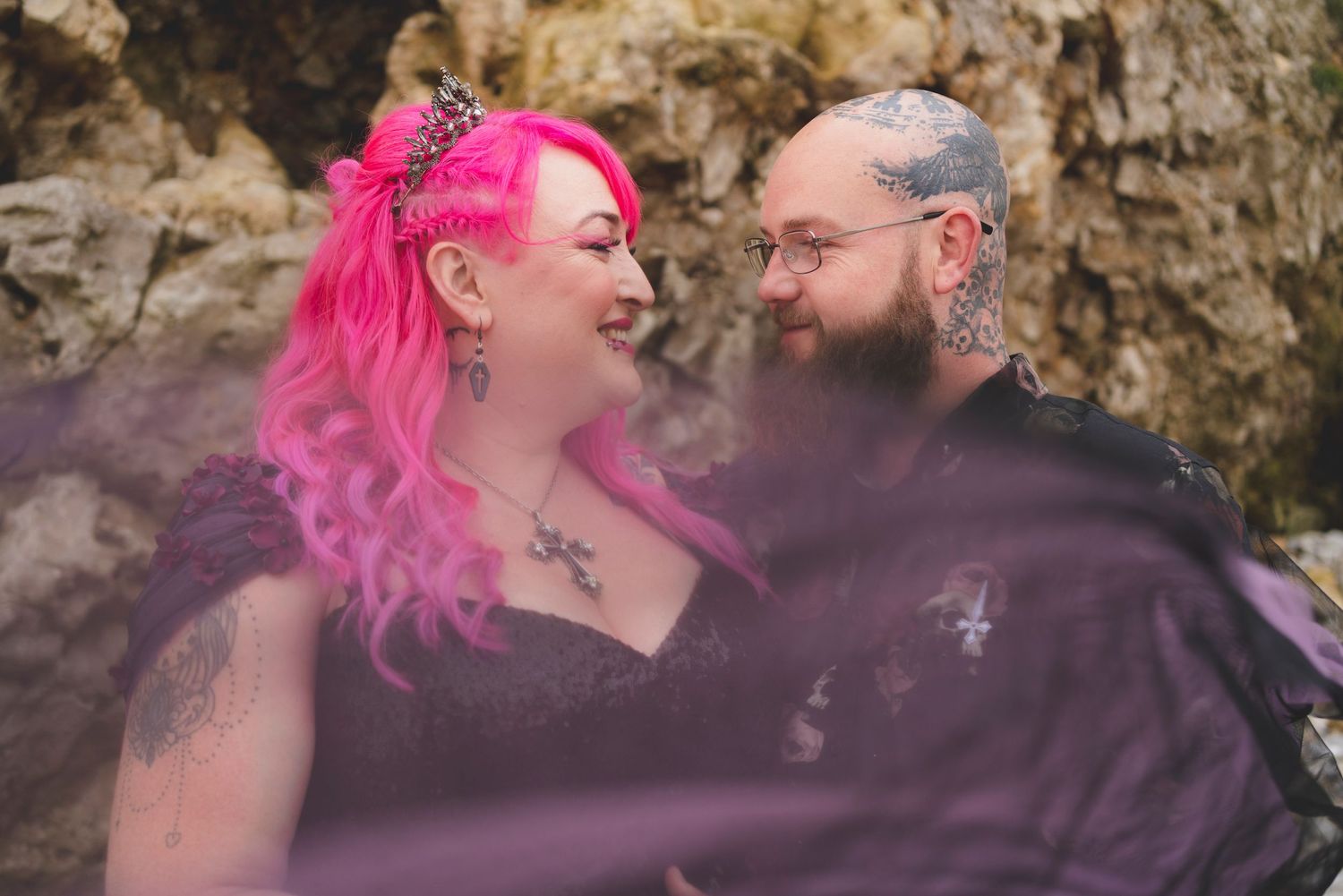 A couple shares an intimate moment against a rocky beach backdrop.