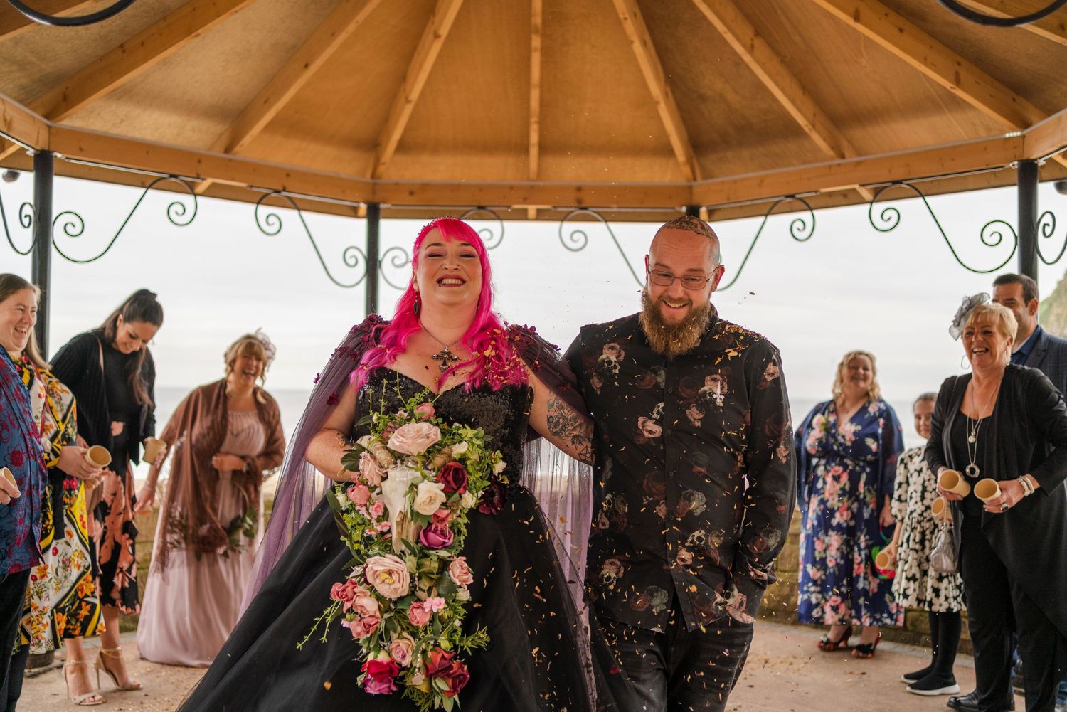 Wedding celebration under a gazebo with confetti falling and guests watching.