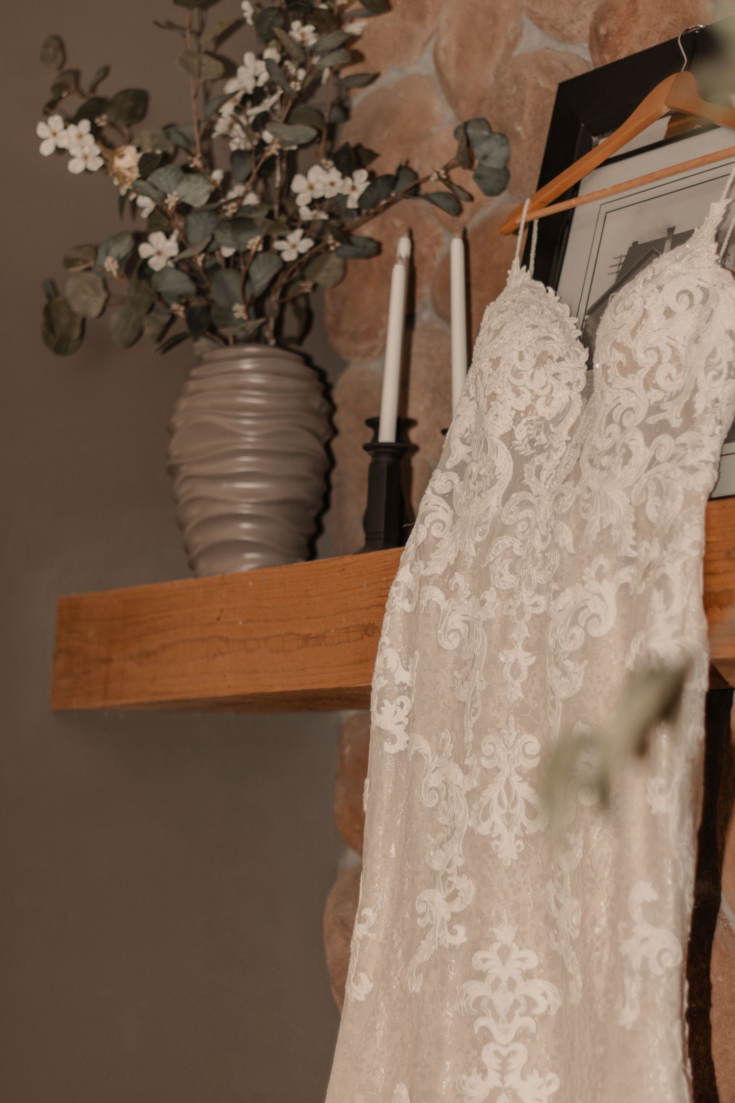 Close-up of wedding dress lace detailing with softly blurred greenery in the foreground, highlights intricate textures.