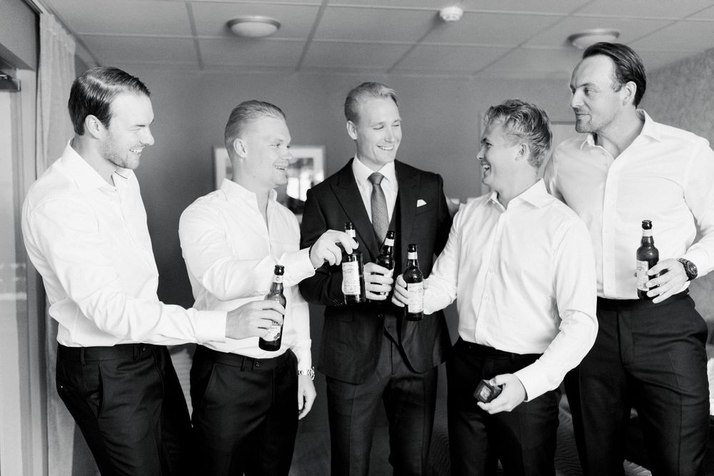 A black and white photo of men in business attire sharing drinks and conversation in an office hallway.