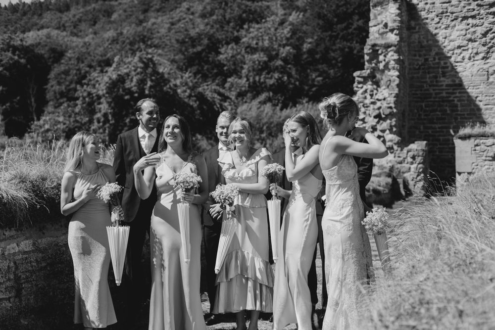 A vintage black and white wedding photo showing a wedding party posing near stone ruins.