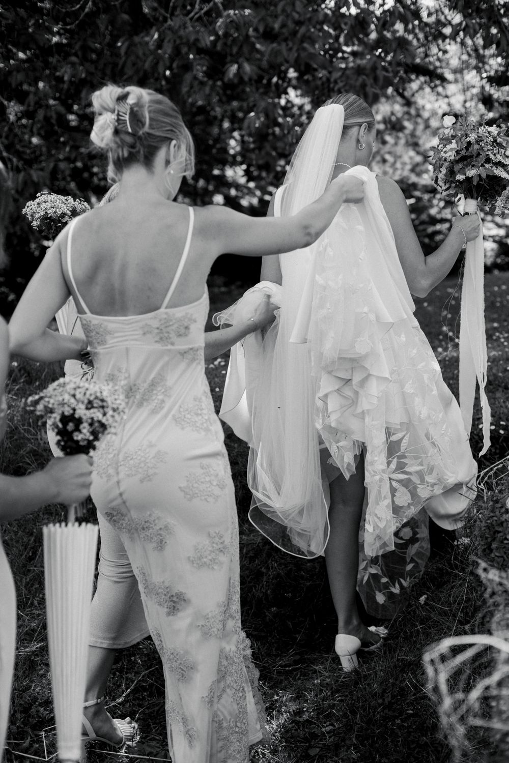 A black and white photo showing a bridesmaid helping adjust a wedding veil.